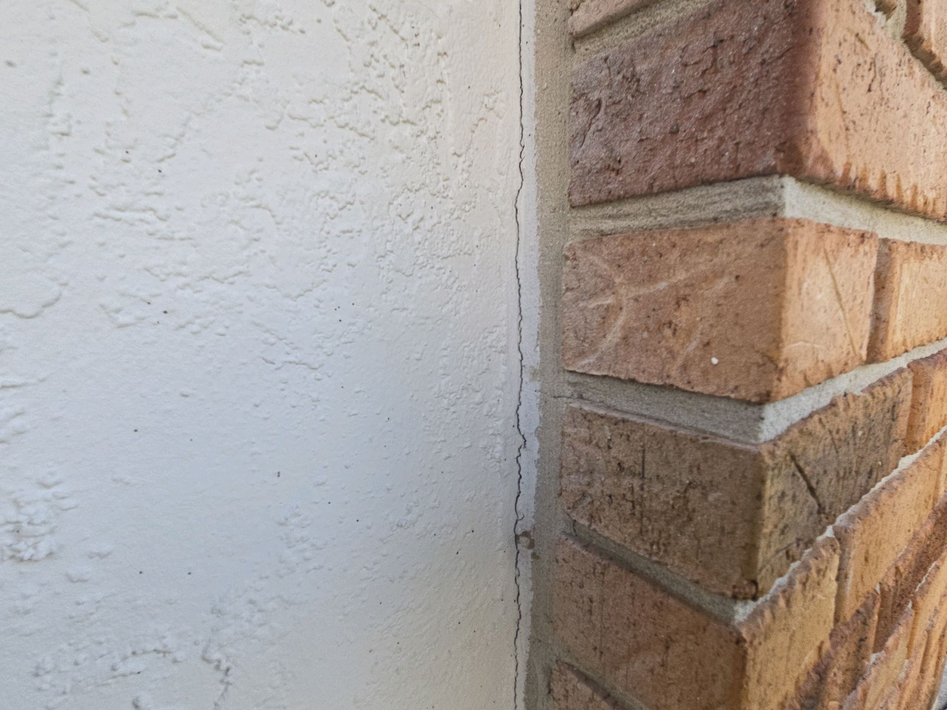 A hairline crack where a stucco wall meets a brick column