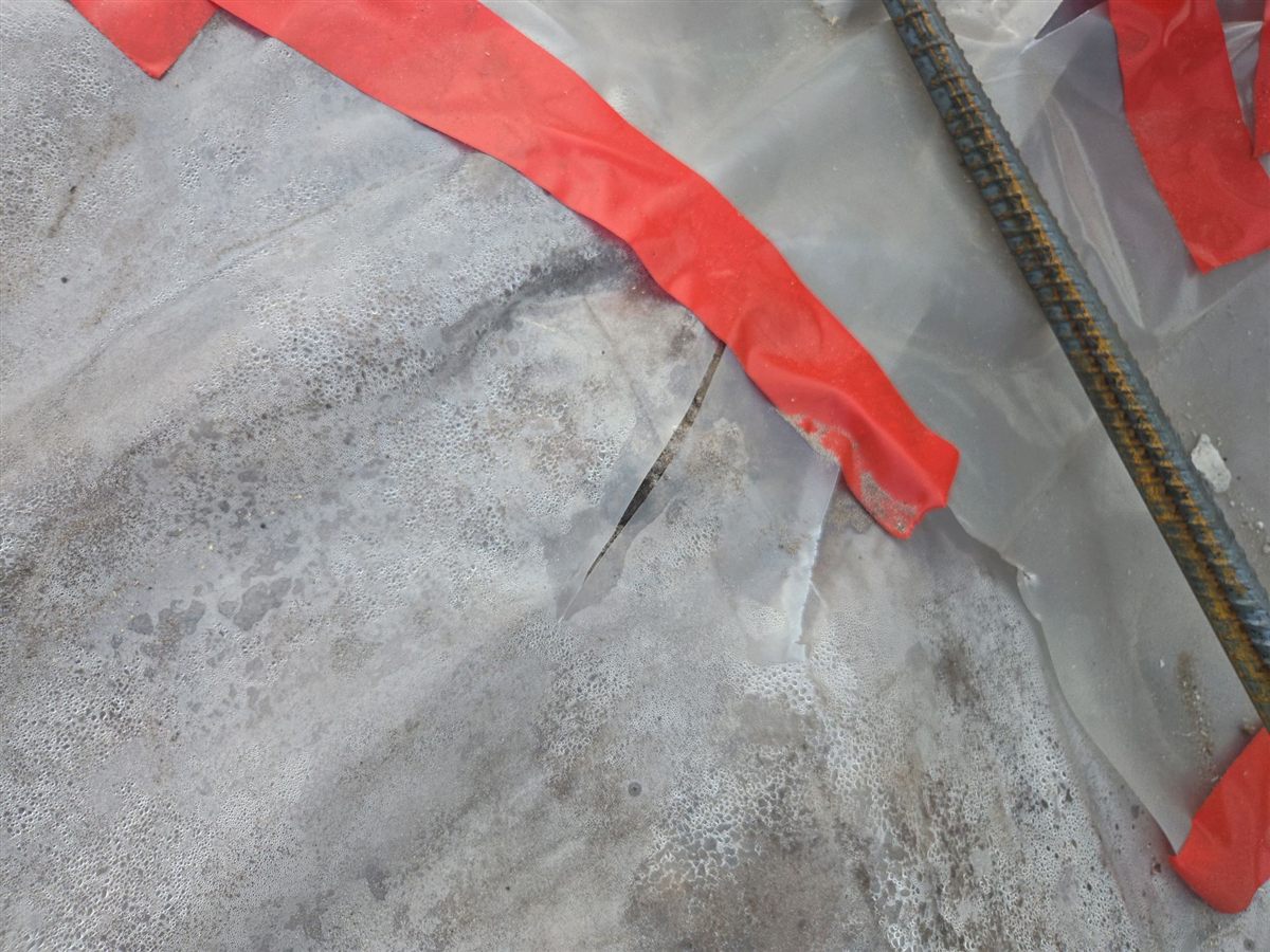 A tear in the vapor barrier beside a rebar dowel, marked with tape for repair before the pour