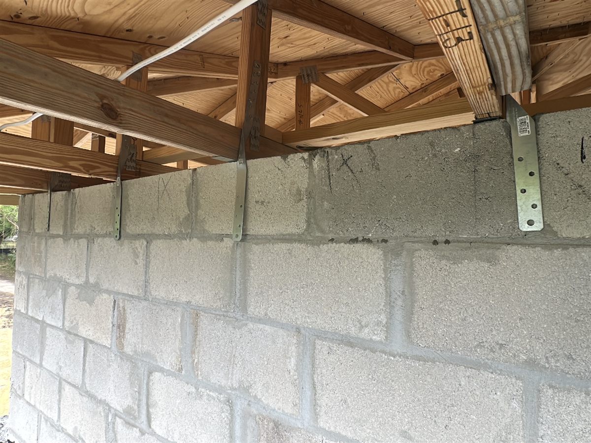 A hurricane strap at the top of a block wall with no fasteners installed into the truss