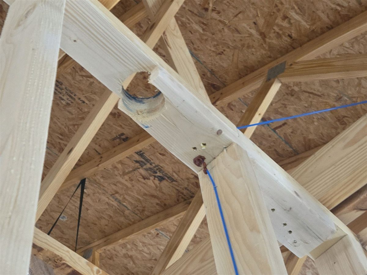 A large opening drilled through a roof truss member near the edge and adjacent to a truss joint