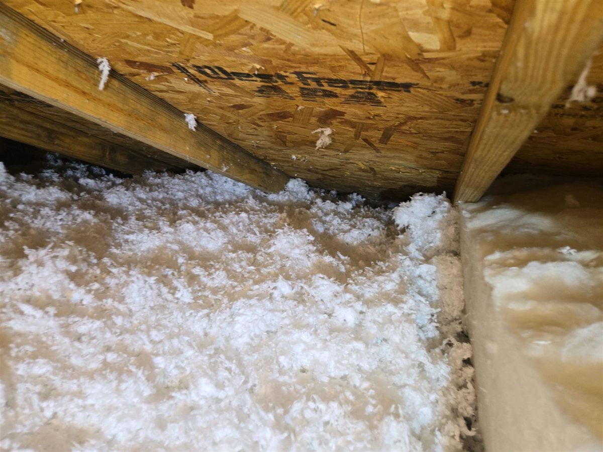 Blown-in attic insulation piled against the underside of the roof deck at the eave, with no ventilation baffle