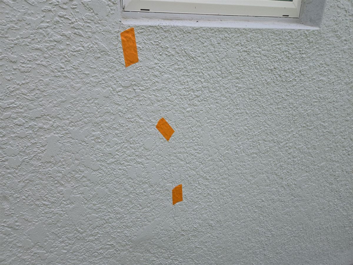 A stucco crack running down from a window corner, marked with tape at the 11-month inspection