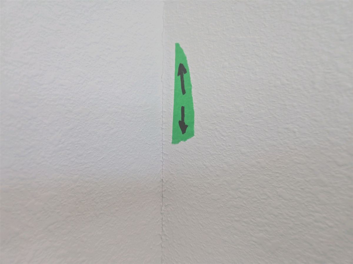 A drywall seam crack at the ceiling, marked with a green arrow