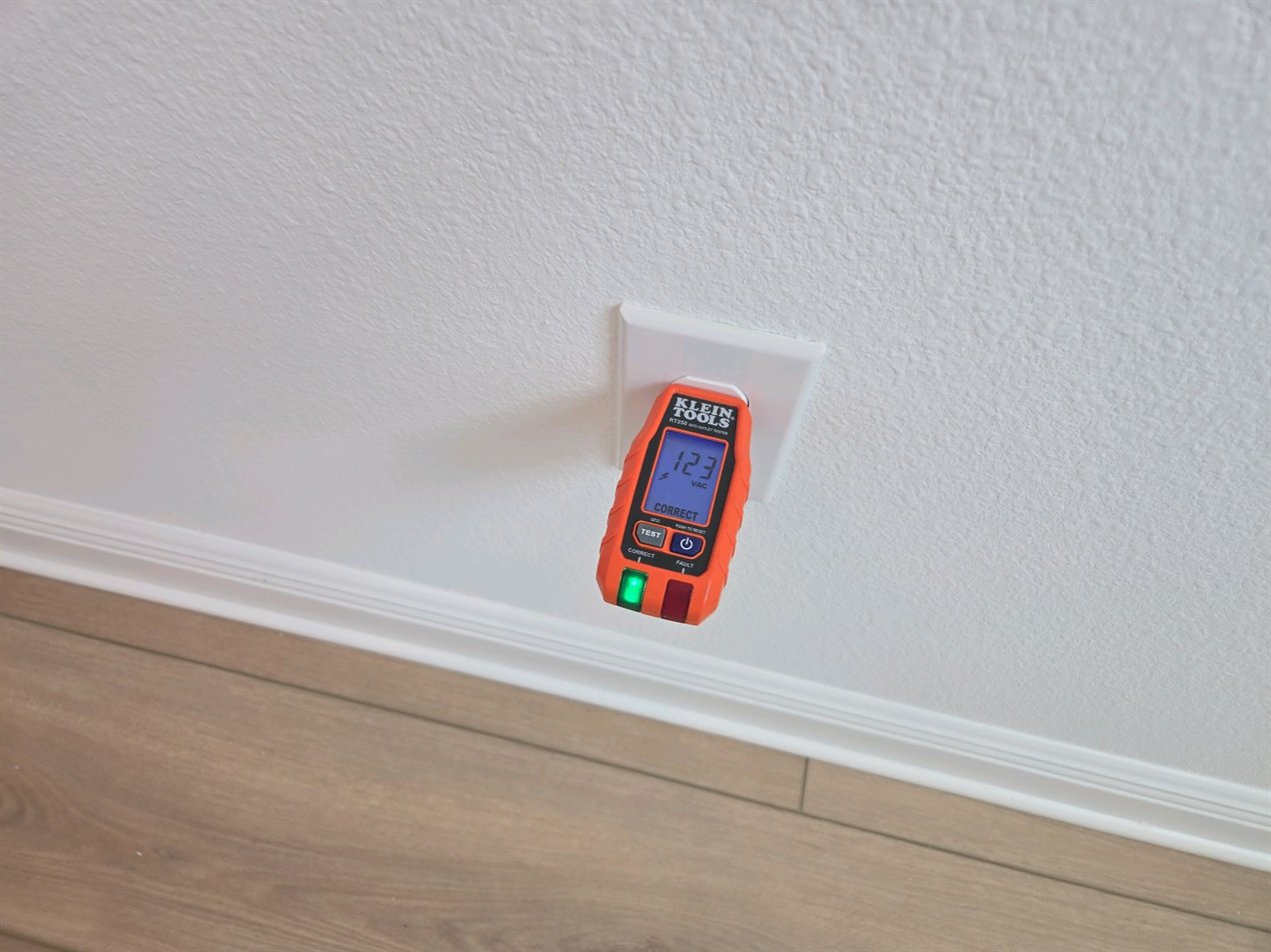 An outlet tester plugged into a receptacle above the baseboard of a finished room, its display reading 123 volts and CORRECT with the green indicator lit