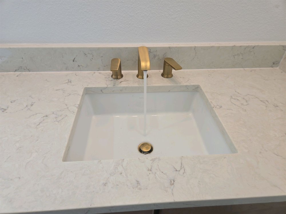Water running from a brushed brass faucet into an undermount bathroom sink set in a quartz countertop