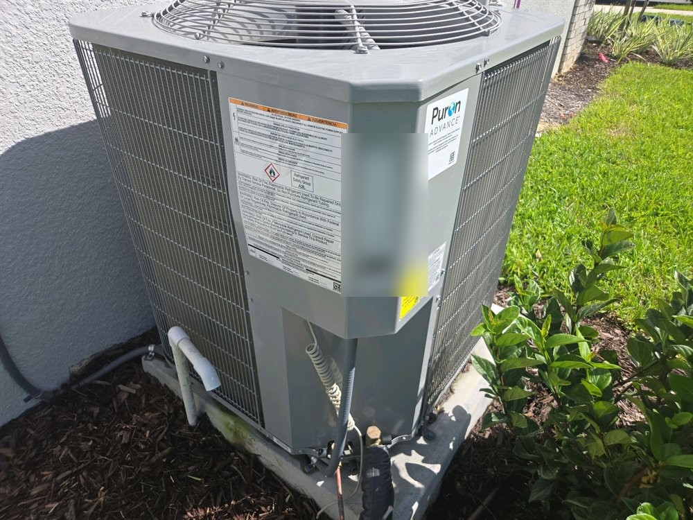 Outdoor air conditioning condenser on its pad beside the house, with the data plate, refrigerant line set and condensate piping visible