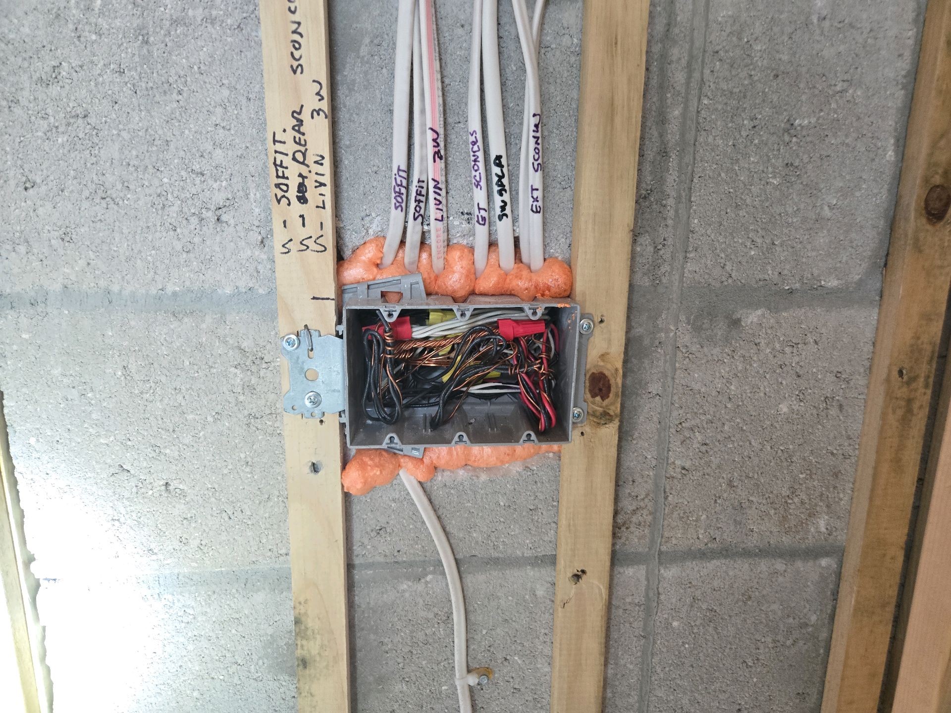 An electrical box on a furred block wall at pre-drywall with each cable hand-labeled