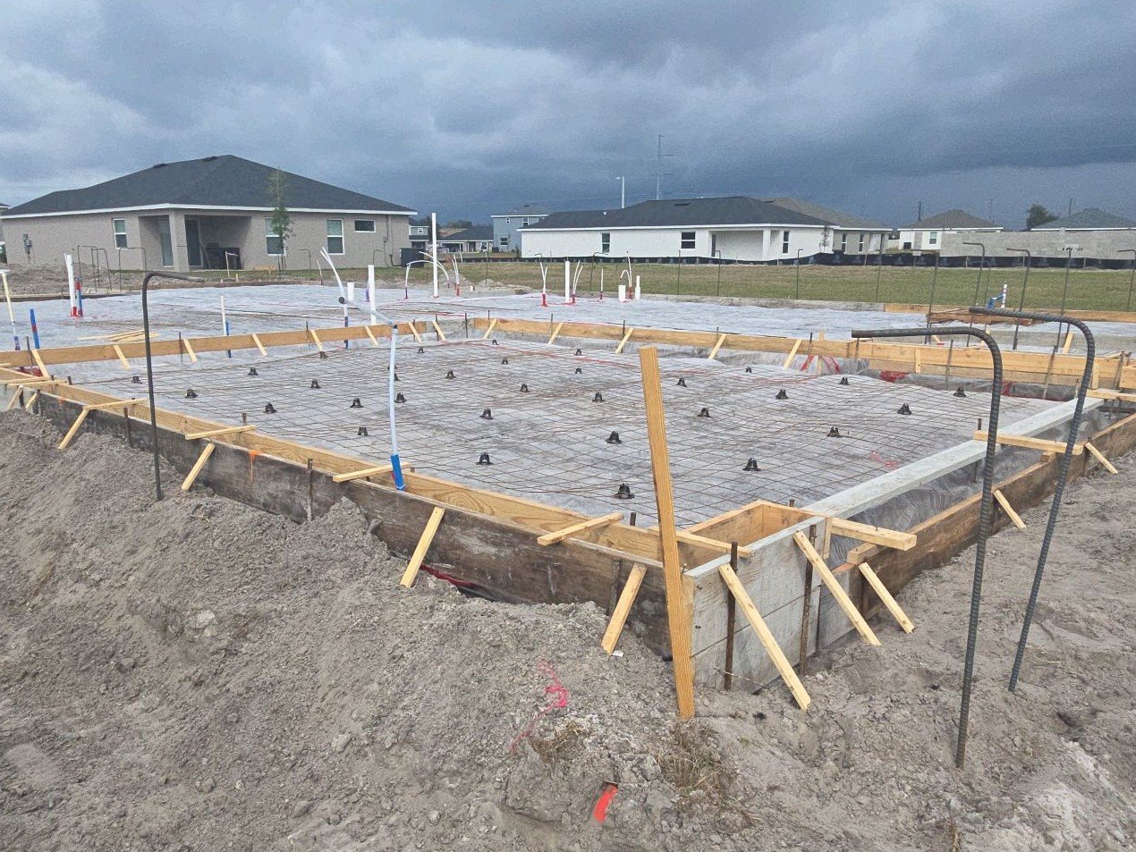 Slab pad before the pour with form boards set, reinforcement mesh raised on chairs, vapor barrier laid, and the perimeter footing trench still open