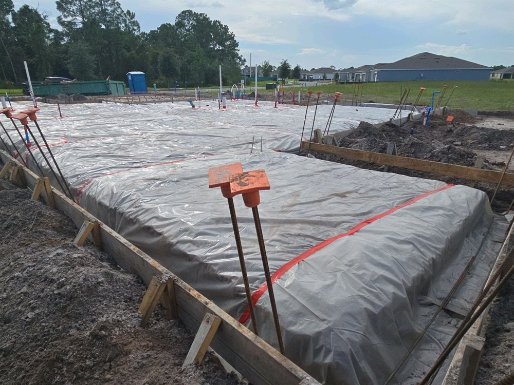 Vapor barrier covering a slab pad with capped reinforcement dowels standing along the perimeter form boards