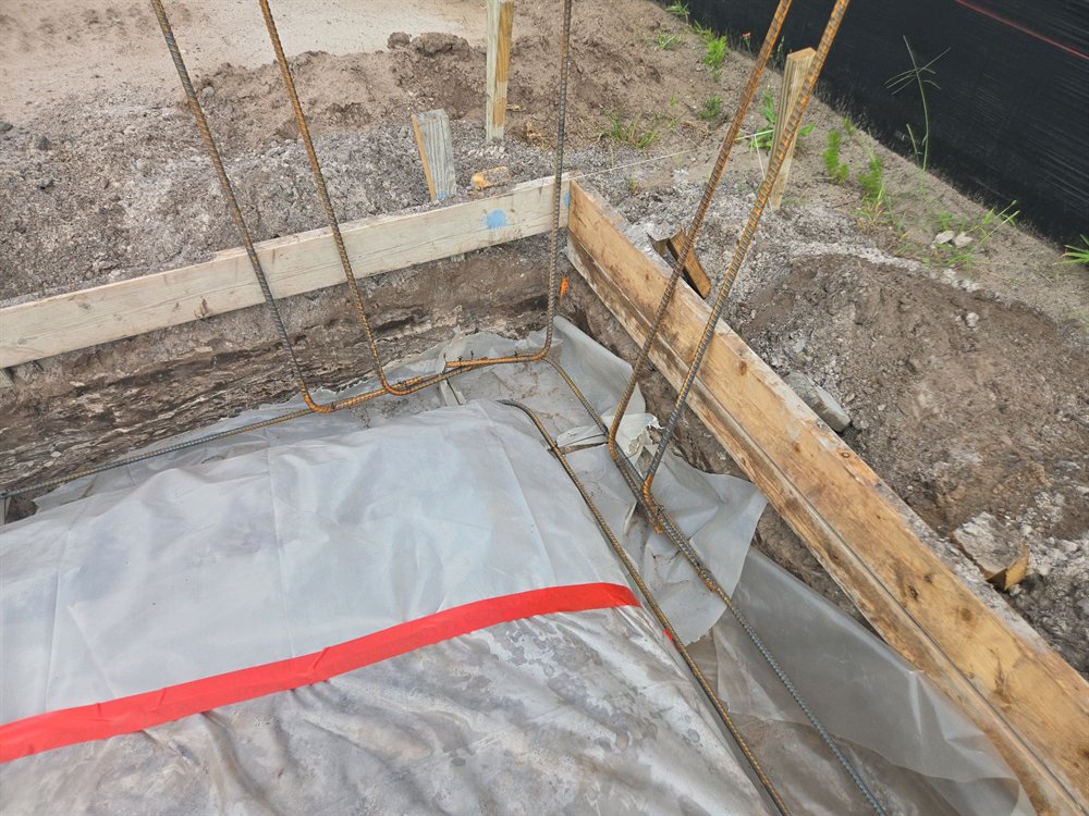 Open perimeter footing trench showing reinforcement hooks and the vapor barrier lapped down into the trench