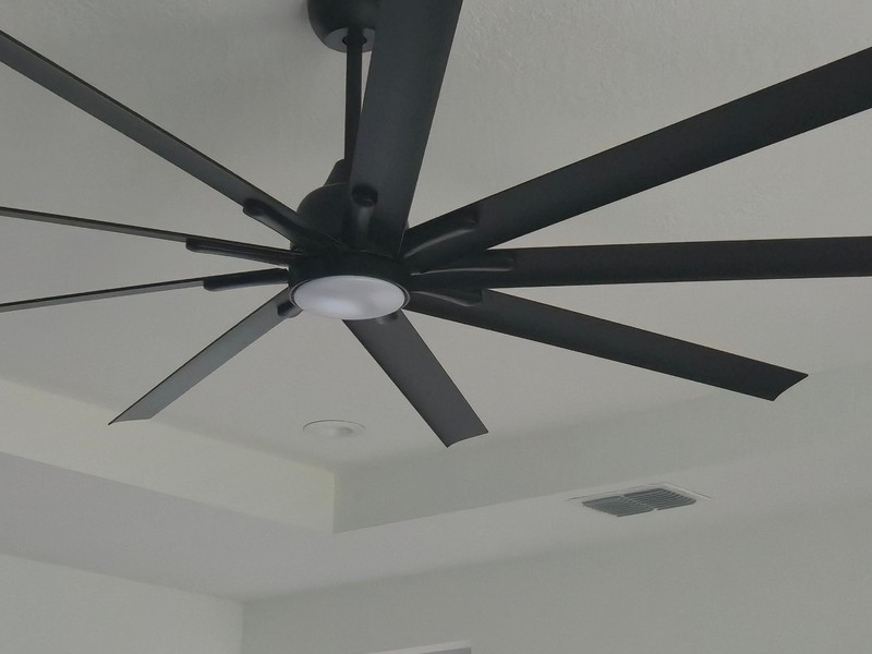 A ceiling fan, tray-ceiling edge and air supply register in a finished living room, as seen by eye.