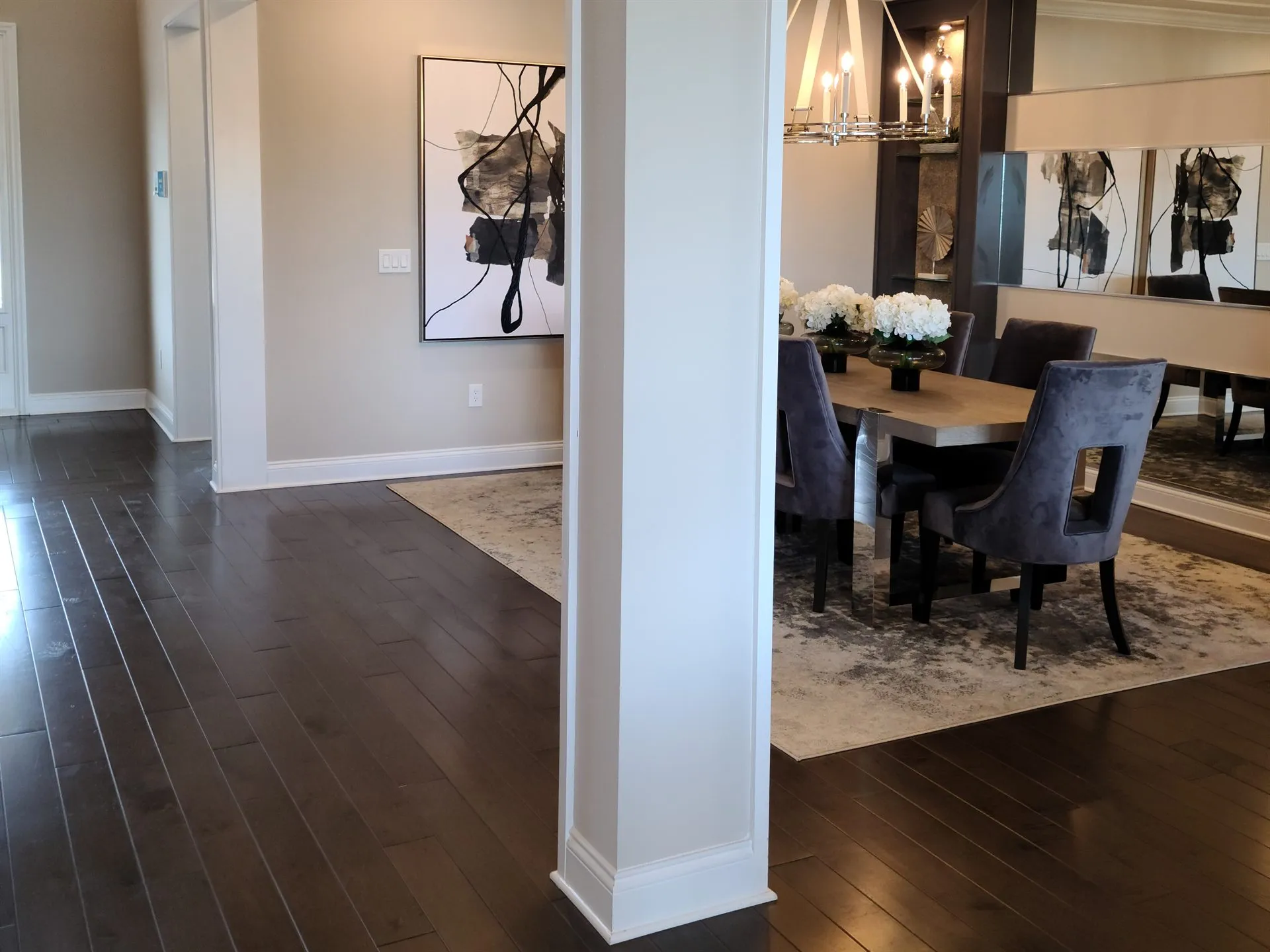 A furnished dining room and hallway with dark wood floors, a square column and a chandelier, about a year after move-in